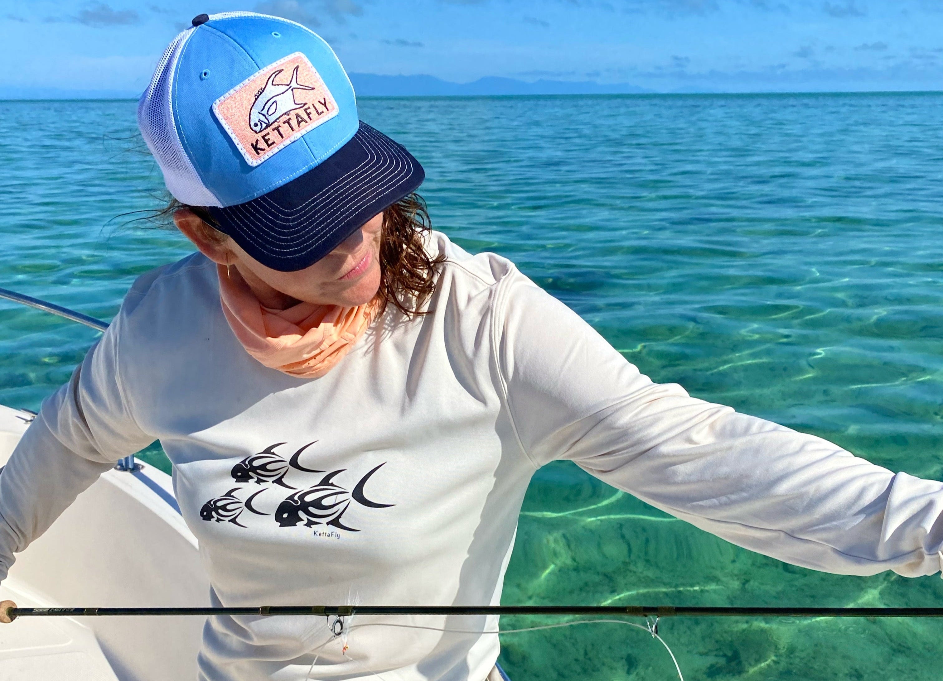 Person on a boat in clear blue water wearing a cap and long-sleeve shirt.